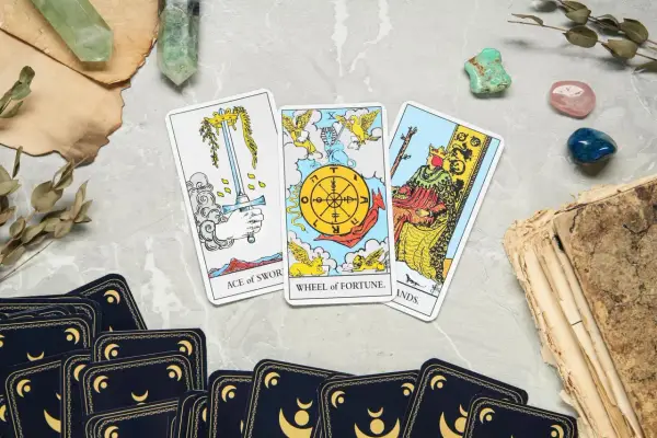Karta życia tarot: As Mieczy, Koło Fortuny i Król Buław. Tajemnicze kryształy i stare księgi dopełniają mistyczną atmosferę.