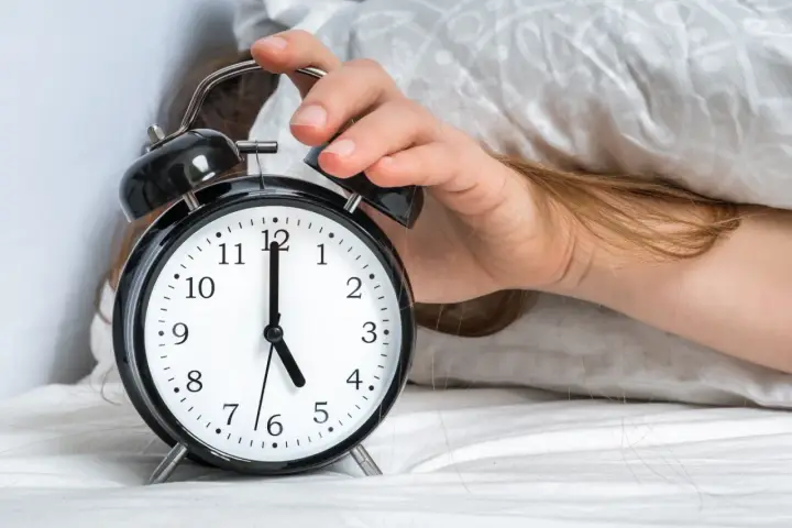 Ręka wyłącza budzik. Jest 5:00, a 0303 znaczenie tego czasu to nowy początek dnia.